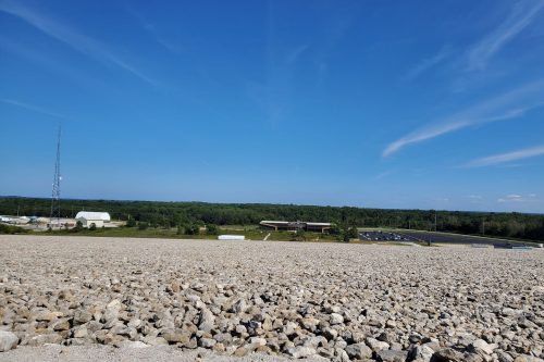 A rocky landscape under a clear blue sky, with a distant building and trees in the background.