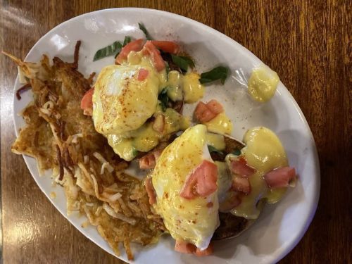 A plate of eggs Benedict with tomatoes on English muffins, served alongside crispy hash browns.