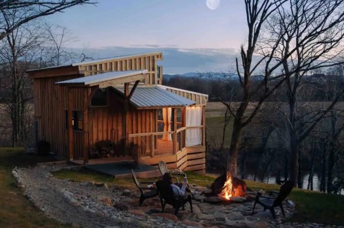 The Little River Tiny House on a hill overlooking the water during the first peaks of nighttime starts to creep across the sky while a roaring fire beckons guests to warm themselves with the glow.