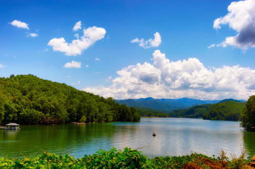 Blue-green water of Nantahala Lake surrounded by trees with blue skys.