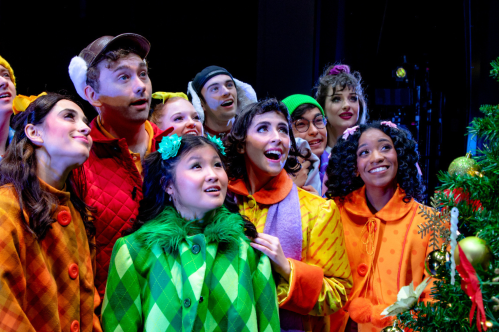 The cast of "A Charlie Brown Christmas Live in Concert." Ten adults in colorful costumes look at a decorated Christmas tree.