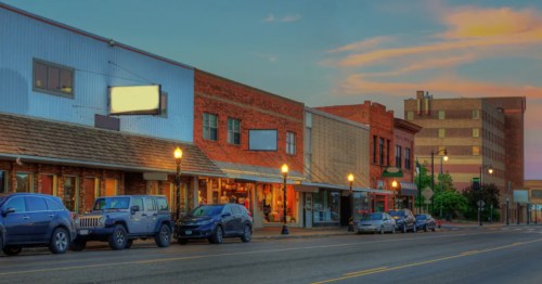 Downtown street in Dickinson, North Dakota at sunset. Brick and painted buildings line the street with cars parked.