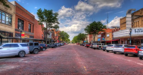 Downtown Kearney, Nebraska, with brick streets, historic buildings, and parked cars under a bright sky.