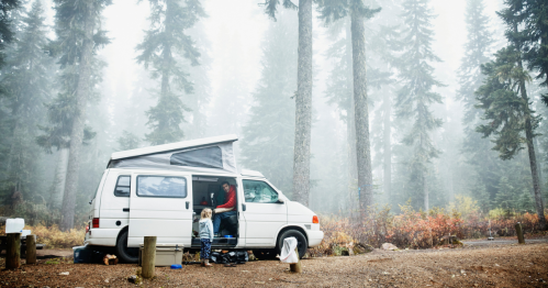 Father sitting in camper van in discussion with young daughter at campsite in woods.