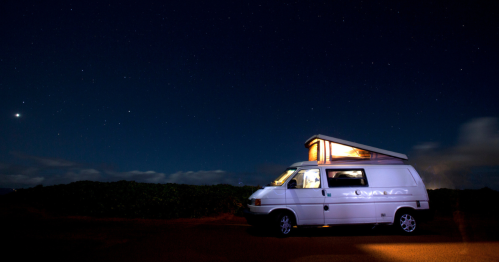 A camper van light up at night beneath a starry sky.