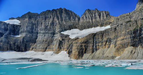 On a clear day, the turquoise waters of Grinnell Glacier Lake sparkle beneath sheer cliffs.