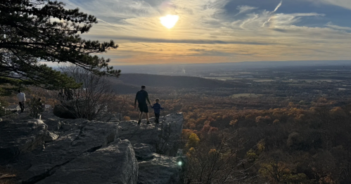 On a rocky outcrop overlooking a vast valley, a father and son take in a sunset.