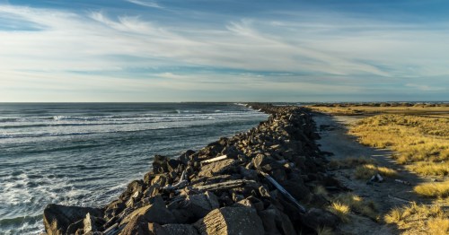 A barrier of rocks and logs separates a grassy area and the ocean at Fort Stevens State Park in Oregon.