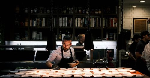 A chef working over a table of food in a dark restaurant.