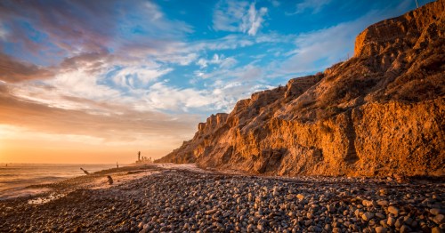 A fiery sunset over a rocky bluff and the Pacific Ocean.