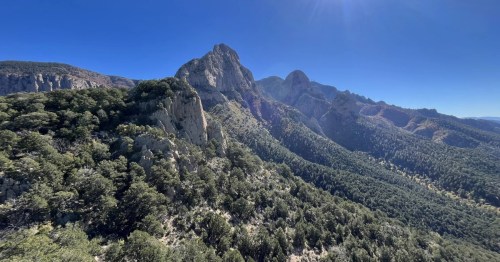 Tall mountain peaks surrounded by a desert landscape on a blue-sky day.