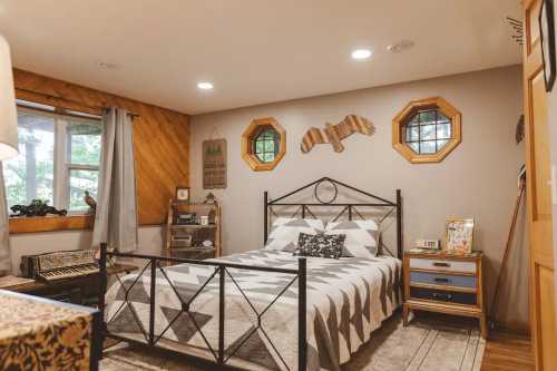 A spacious bed and a gray and white patterned quilt sits in the middle of a bedroom with octagonal windows and rustic elements.