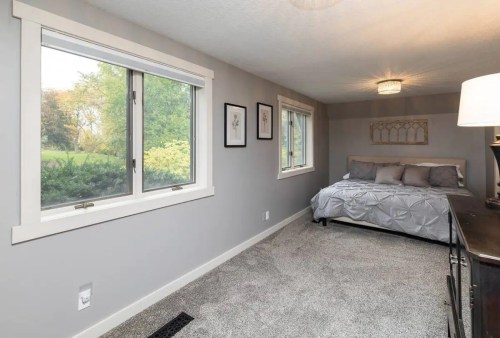 A large gray-scale bedroom with a single bed and two windows looking out into nature.