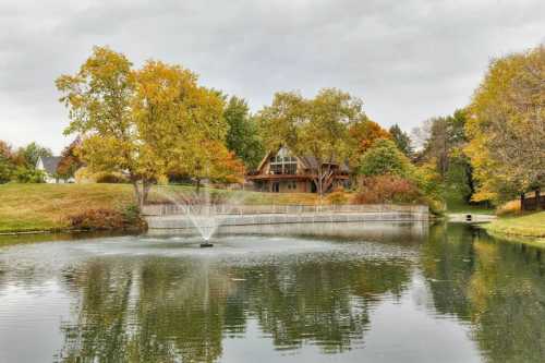 A large lake with a fountain sits before a massive cabin surrounded by Iowa fall foliage.