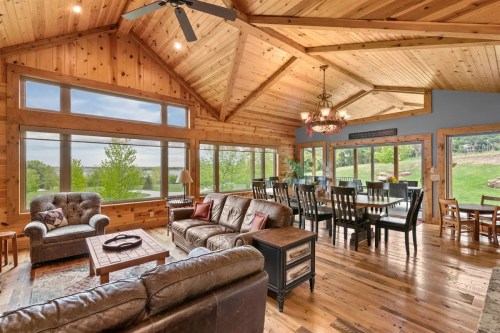 A gorgeous cabin room with a couch and dining space is framed by wide windows overlooking a verdant Nebraska landscape.