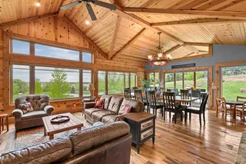 A gorgeous cabin room with a couch and dining space is framed by wide windows overlooking a verdant Nebraska landscape.