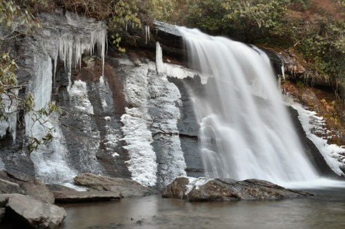 Silver Run Falls as the water cascades on one side in a wintery wonderland and the other side of the falls has frozen over leaving a layer of long icicles and snow.
