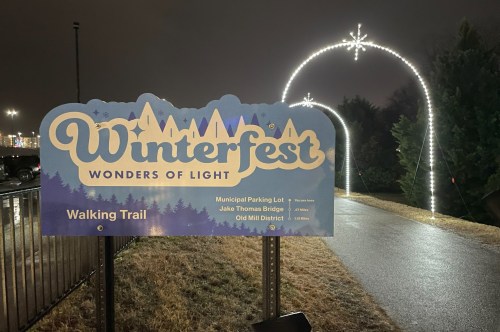 The entrance of the Winterfest Wonders of Lights Walking Trail with a festive blue sign and arched lights lining the path.