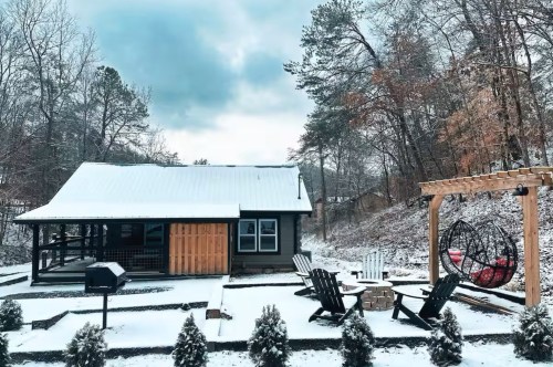 A snowy day with a dark cabin and all the trees around it covered white fluffy snow.