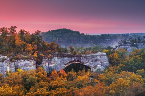 A classic scenic view of an arch found in Daniel Boone National Forest in the fall as the sun sets creating beautiful blue and purple hue in the sky.