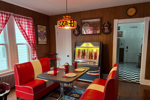 The dining room at the "CT Pizza Palace" Airbnb in New Haven, CT. The pizza-themed room has two vintage restaurant seats, a "Pizza Hut" chandelier, and a jukebox.