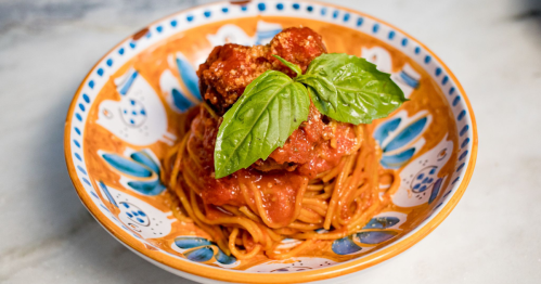 A fresh plate of pasta al pomodoro is served in a colorful bowl and garnished with fresh basil.