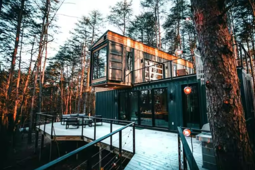 A snow-covered deck leads to a modular-style cabin in the Ohio woods.