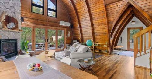 The living room of a cabin rental near Mount Hood, Oregon, is complete with vaulted ceilings, large windows, a couch, a fireplace, and a dining area.