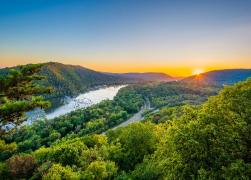 Sunset view of the Potomac River from Weverton Cliffs near Harpers Ferry, West Virginia, with warm light over the river and surrounding landscape.