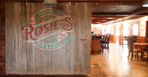 The rustic wood entrance to Rosie’s Bar & Grill in WaKeeney, Kansas, featuring a hand-painted floral logo.