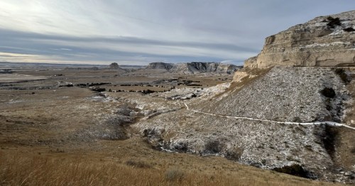 Snowy trail winding up a dramatic bluff face overlooking the vast, brown Nebraska prairie landscape.