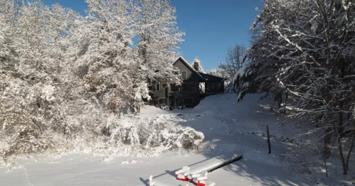 An elevated view of a dark gray, modern cabin nestled among snow-covered trees, overlooking a frozen lake with a dock in Amery, Wisconsin.