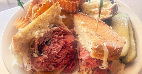 an overstuffed reuben sandwich sits on a lpate with a side of chips and cole slaw