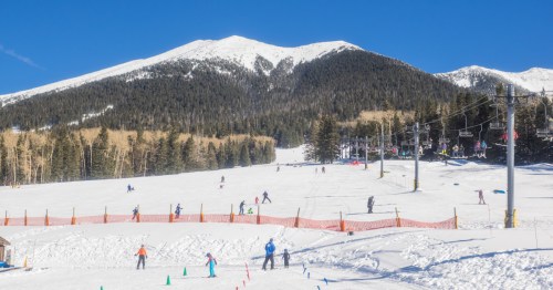 view of mount humphreys in the background and skiers on the snowy ski hills in flagstaff az