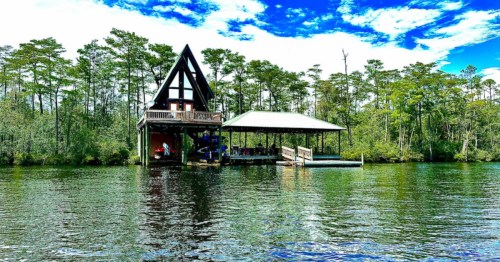 A waterfront A-frame cabin in Alabama with a lush treeline behind it.