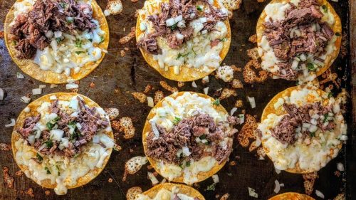 A tray of crispy tortillas topped with melted cheese, shredded beef, and diced onions, ready to serve.