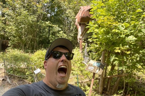 A man screams in absolute terror as a looming T-Rex breaks through the trees in hot pursuit.