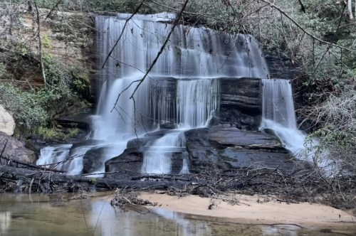 The cascading white flow of the waterfall matches perfectly with the slightly snowy ground and snow-covered branches.