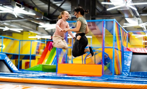 two young girls jumping together on colorful trampoline at and indoor playground park