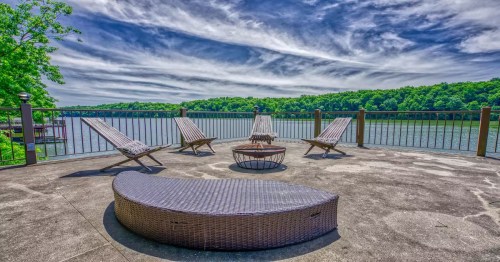 Four chairs on a patio that overlooks a body of water with cloudy skies and green trees in the background.