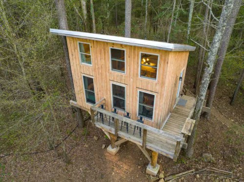A two-story cabin sitting amongst the forest and large green trees in Arkansas