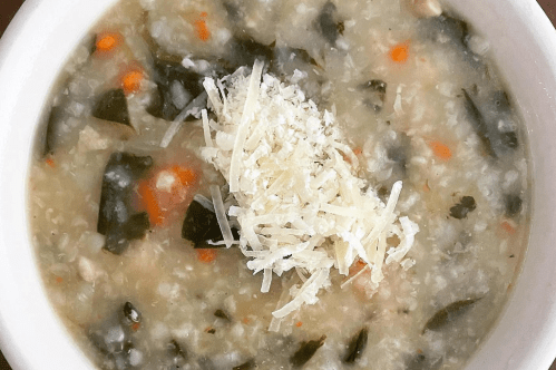 Close up photo of chicken and rice soup with vegetables and cheese on top.