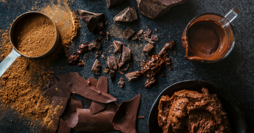 An overhead view of chocolate chunks, chocolate frosting, cocoa powder, and chocolate syrup.