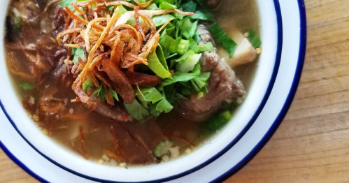 Delicious-looking oxtail soup is served in a white enamel bowl with navy blue edges.