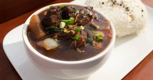A bowl of rich beef stew is served alongside rice.