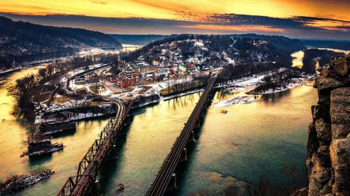 A scenic view of a river and bridges at sunset, with a small town nestled along the water's edge.