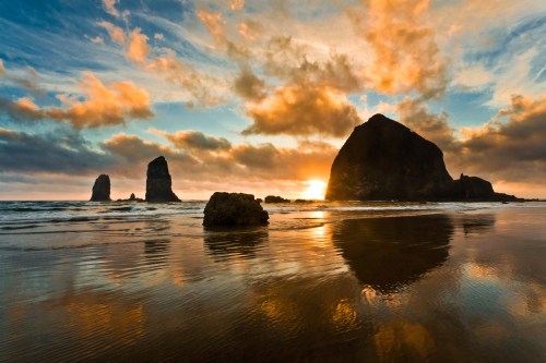 Haystack Rock rising from the ocean near the shoreline, a well-known coastal landmark.