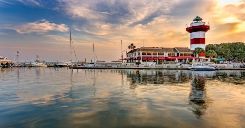 Lighthouse on Hilton Head Island lays atop a peaceful harbor with a sunset in the background.
