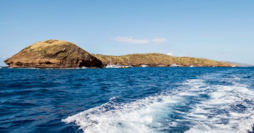 Scenic boat view of Molokini Crater's crescent volcanic islet in Maui, surrounded by deep blue Pacific waters.
