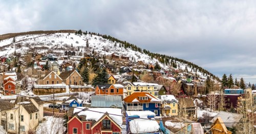 Colorful mountain homes in Park City, Utah with cloudy sky background in winter. Leafless trees and conifers grows on the snow covered neighborhood.